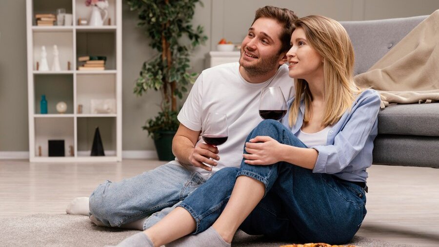 Fiatal pár pizzával és borospoharakkal ül a földön és filmet néznek. Fiatal pár pizzával és pohár borral a földön ülve filmet néznek